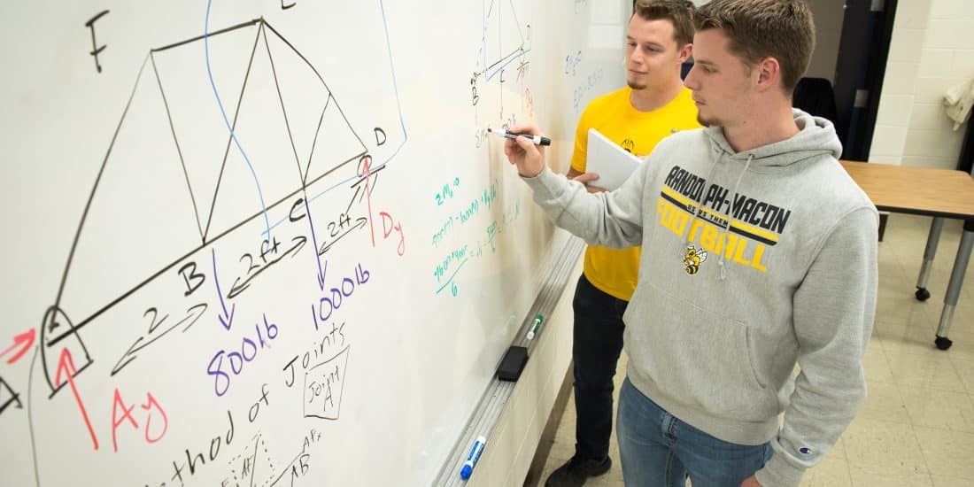 Two physics students figuring out equations on a white board