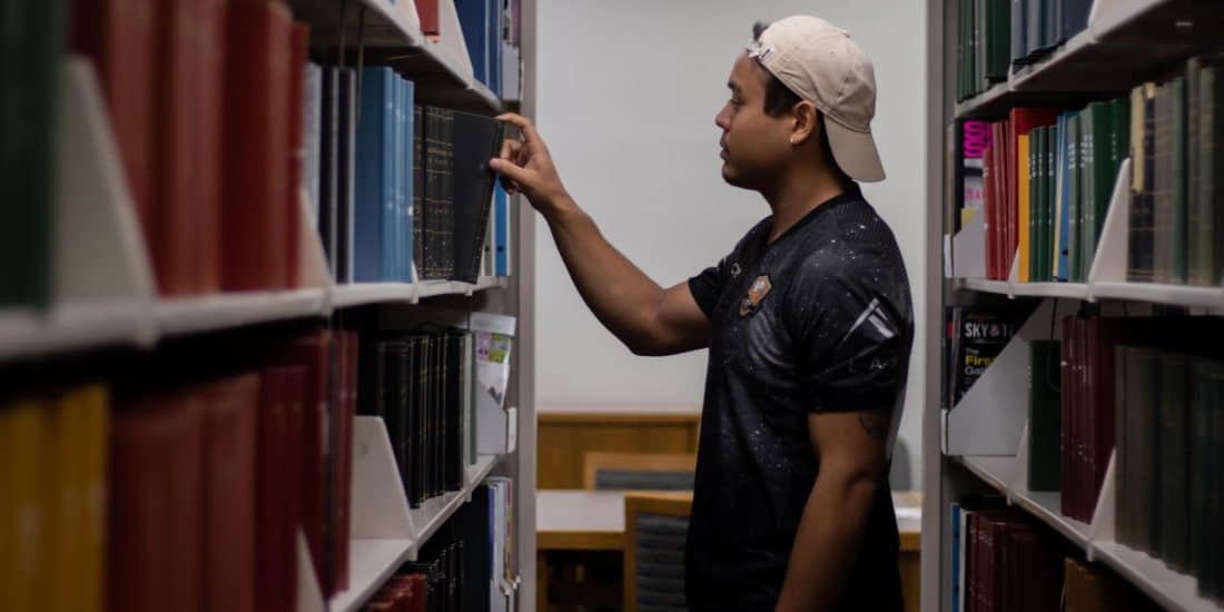 Student pulling a book from a library bookshelf