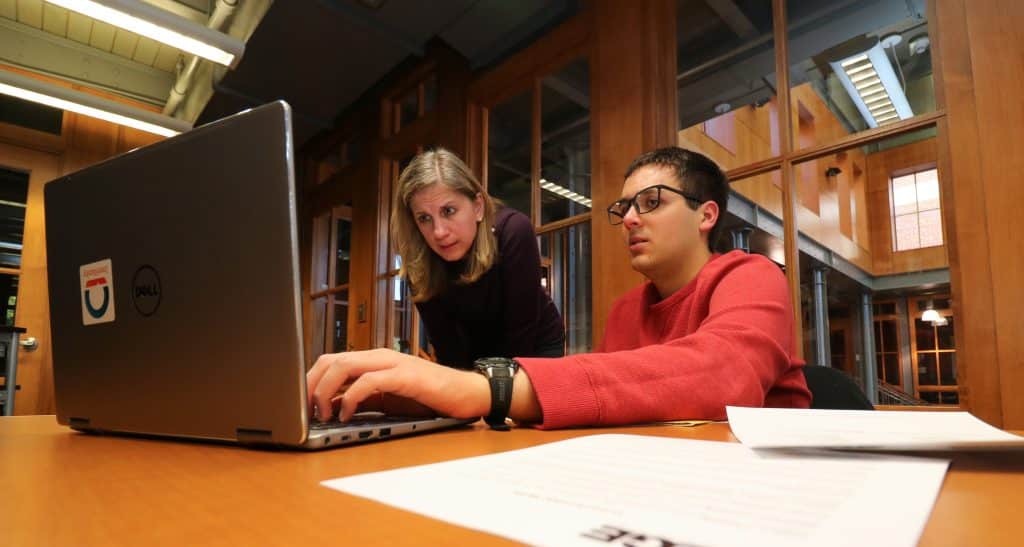 A ӣֱ employee guides a student working on a laptop during a resume writing workshop in the Edge Career Center