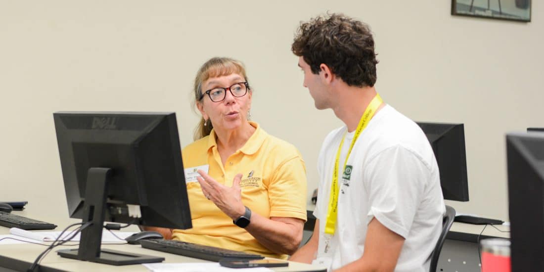 A faculty member and student converse in front of a computer.