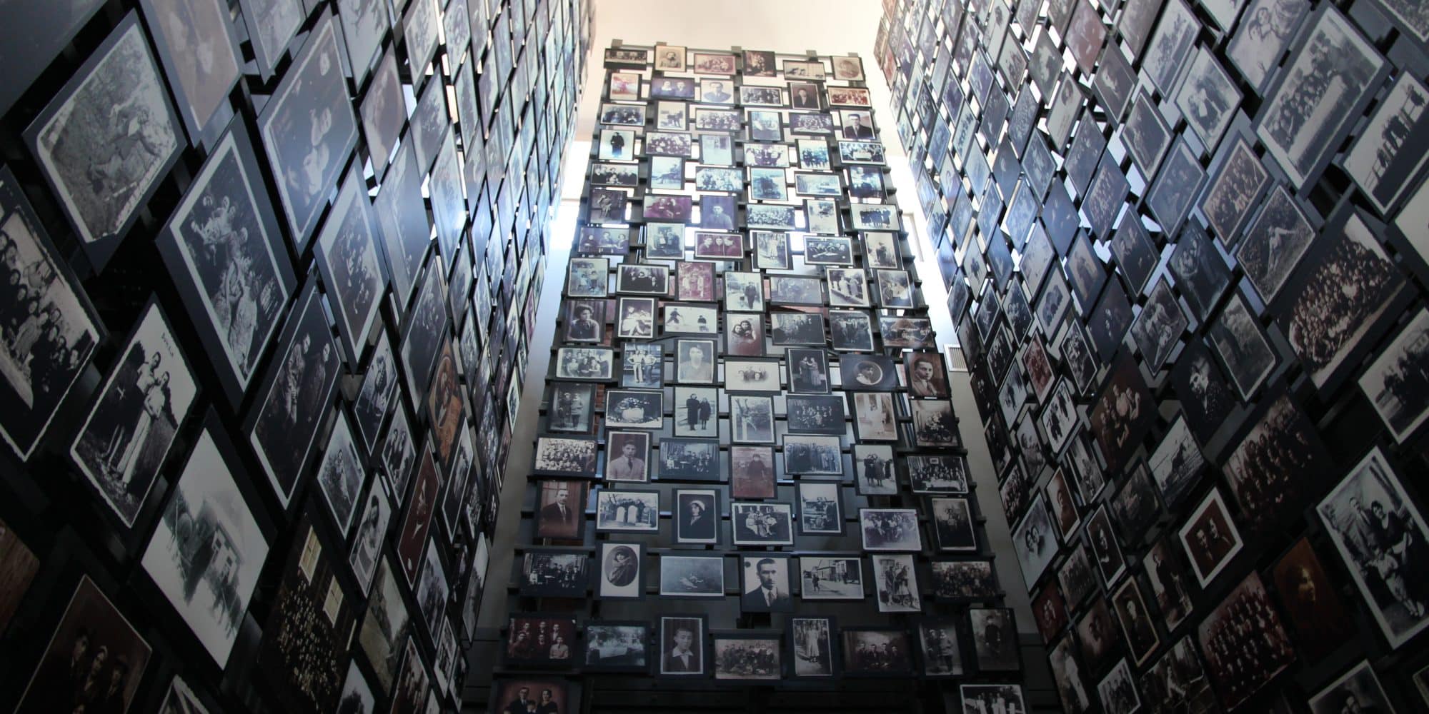 A view looking up at a towering atrium wall filled with numerous framed photos in black and white, under a clear skylight.